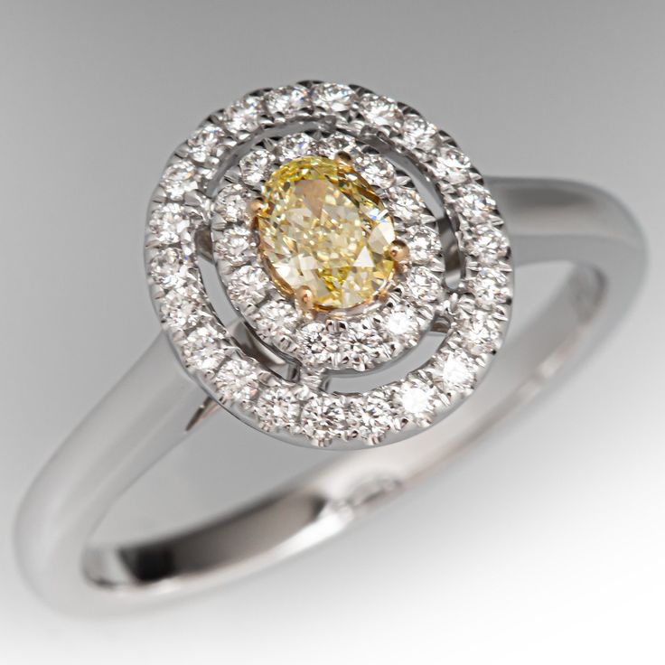 an oval shaped yellow diamond surrounded by white diamonds in a halo setting on a silver ring