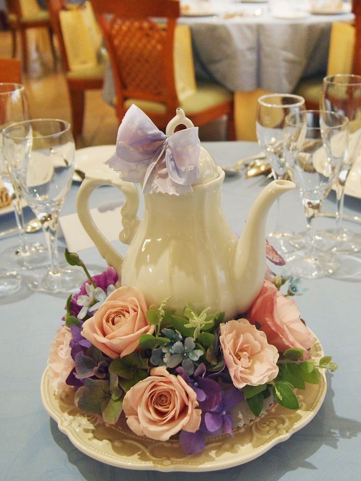 a white tea pot with pink roses and purple hydrangeas sits on a blue table cloth