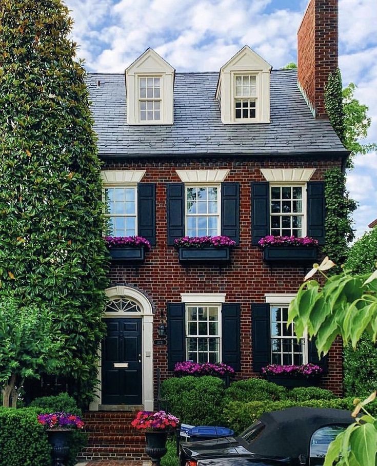 a large brick house with black shutters and flowers on the front window sill