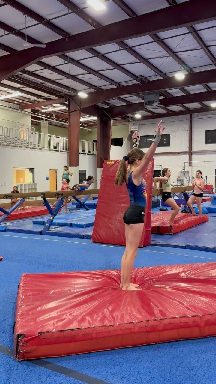 a woman is standing on top of a trampoline in an indoor gym with other people