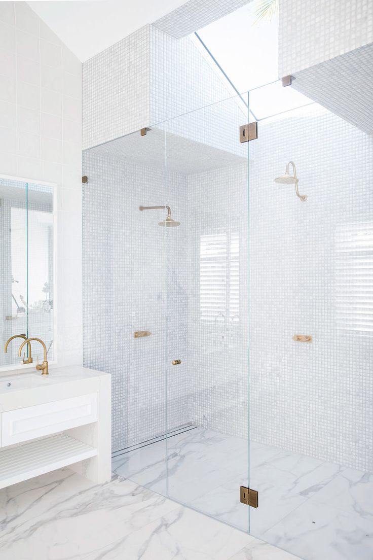 a white bathroom with marble counter tops and glass shower doors that are open to reveal a walk in shower