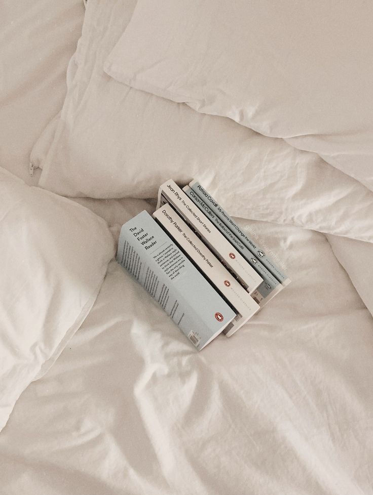 a stack of books sitting on top of a bed covered in white sheets and pillows