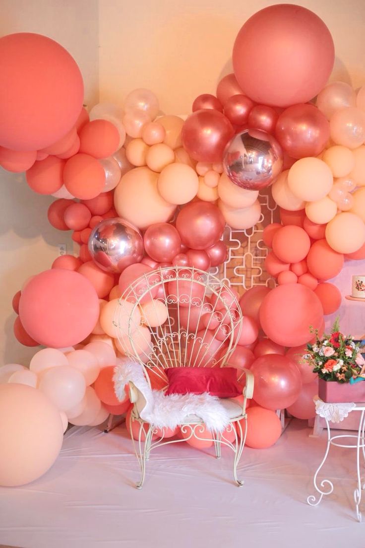 a room filled with balloons and furniture next to a wall covered in pink, white and gold