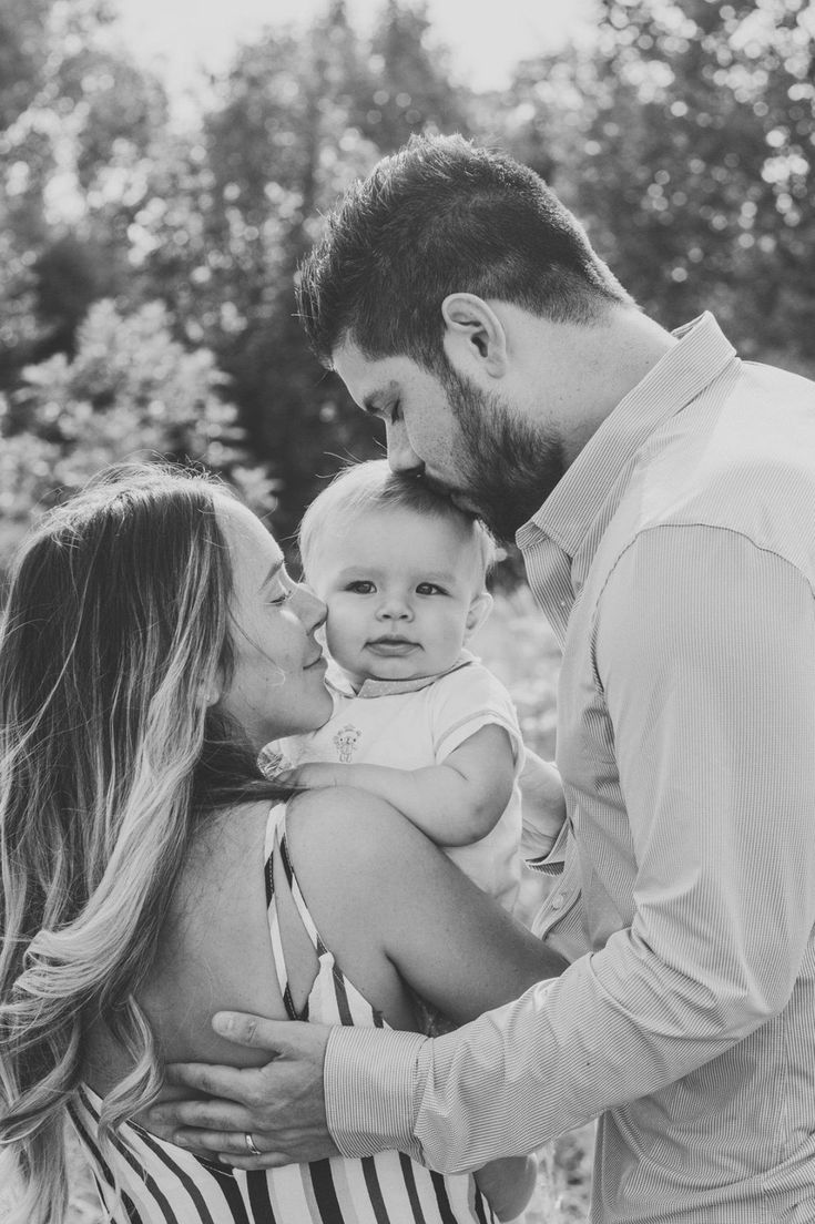 a man holding a baby in his arms while standing next to a woman with her arm around him