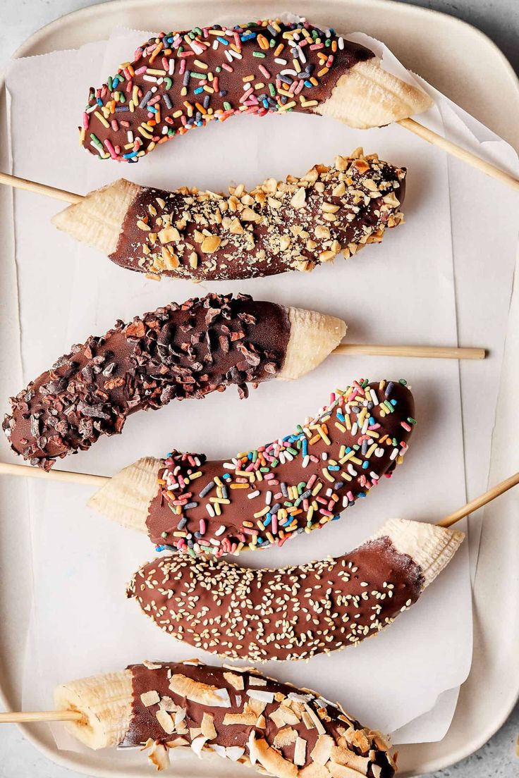 five chocolate covered donuts on sticks with sprinkles