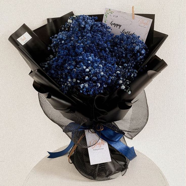 a bouquet of blue flowers is wrapped in black paper and tied to a white pedestal