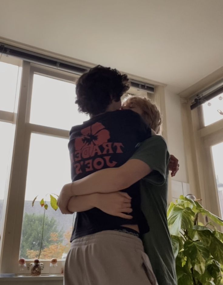 two people hugging each other in front of a window