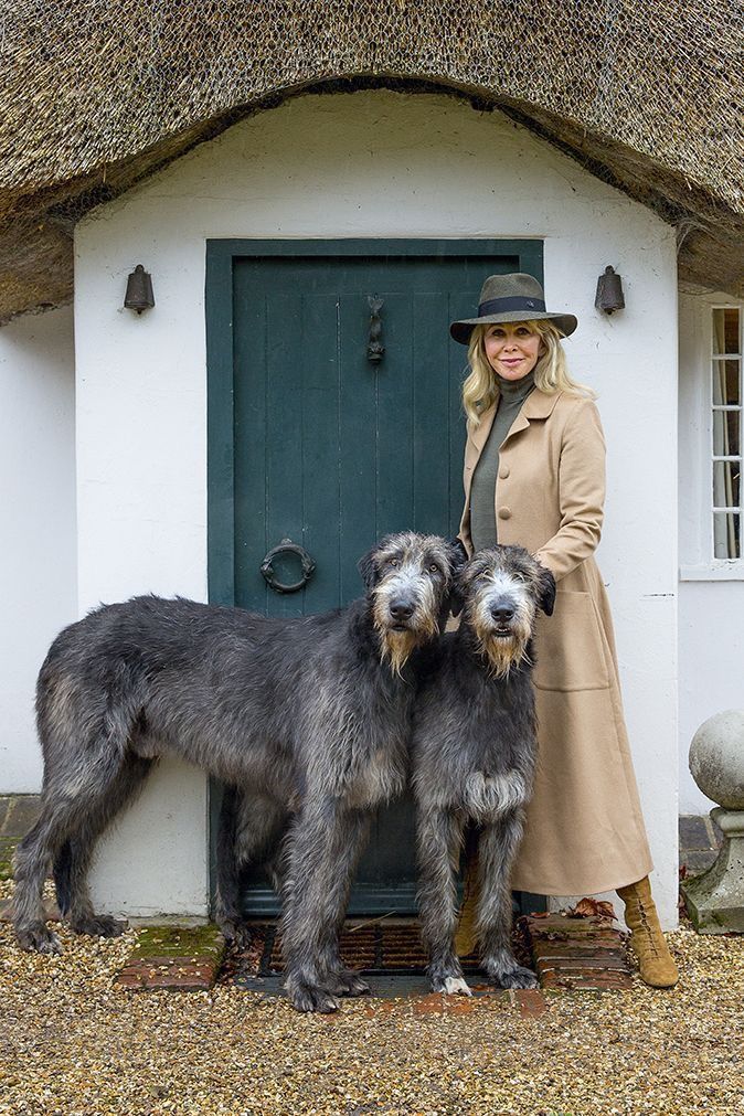 a woman standing next to two dogs in front of a white house with thatched roof