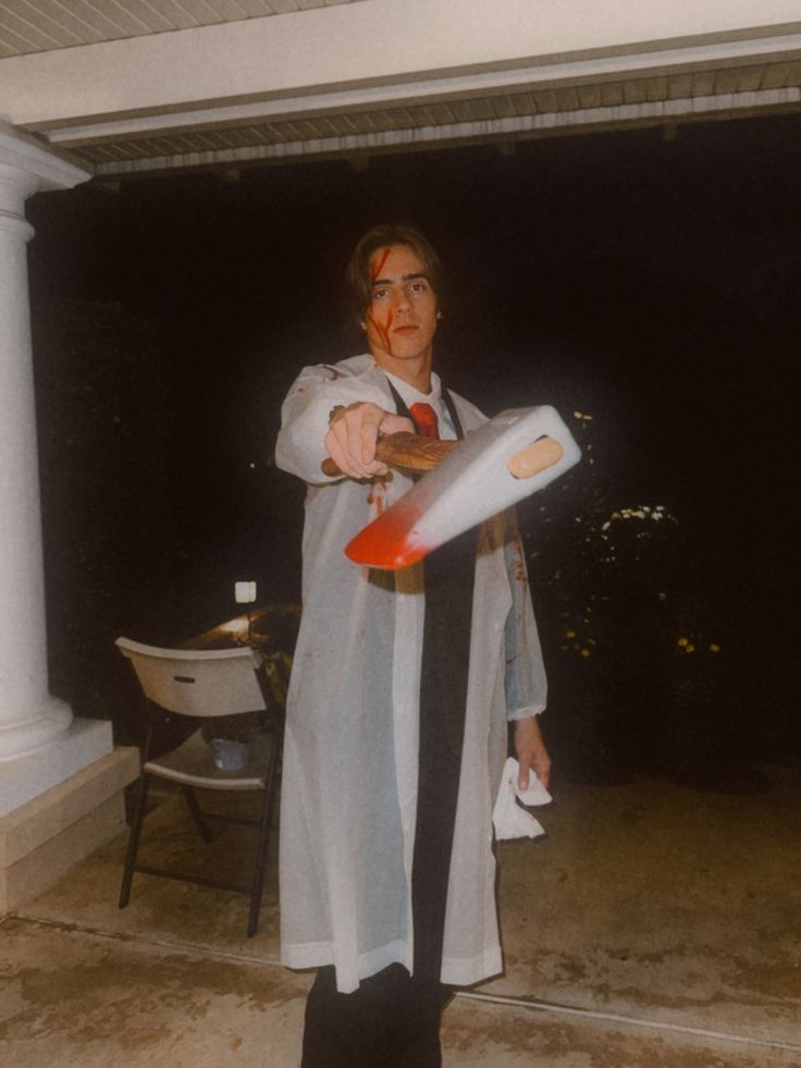 a man in costume holding a frisbee on the porch at night with blood all over his face