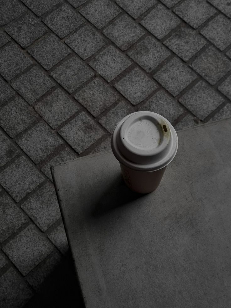 a coffee cup sitting on top of a cement table next to a sidewalk with cobblestones