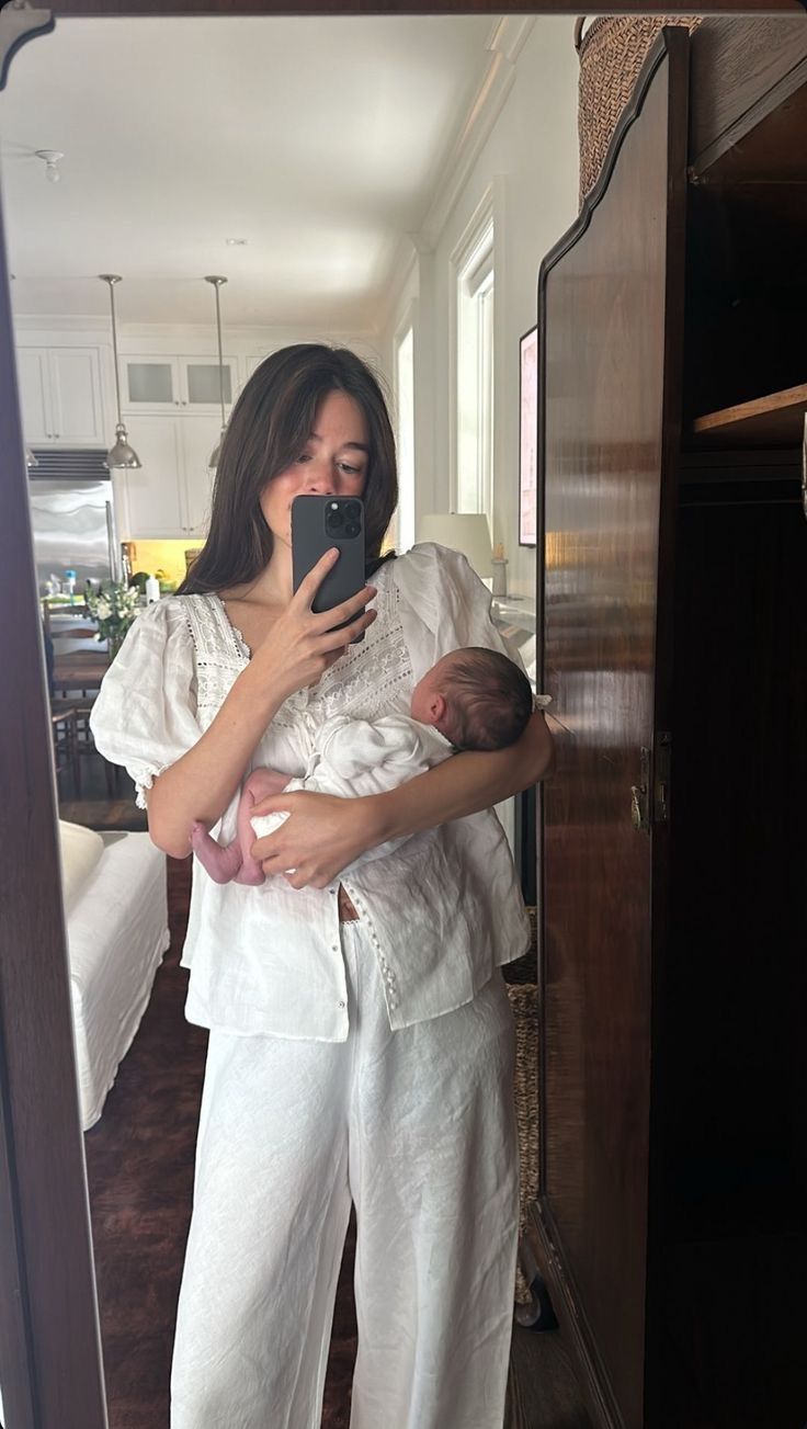 a woman holding a baby in her arms taking a selfie with the mirror behind her