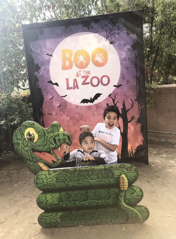 two children sitting in a fake green snake chair with the sign boo at the la zoo behind them