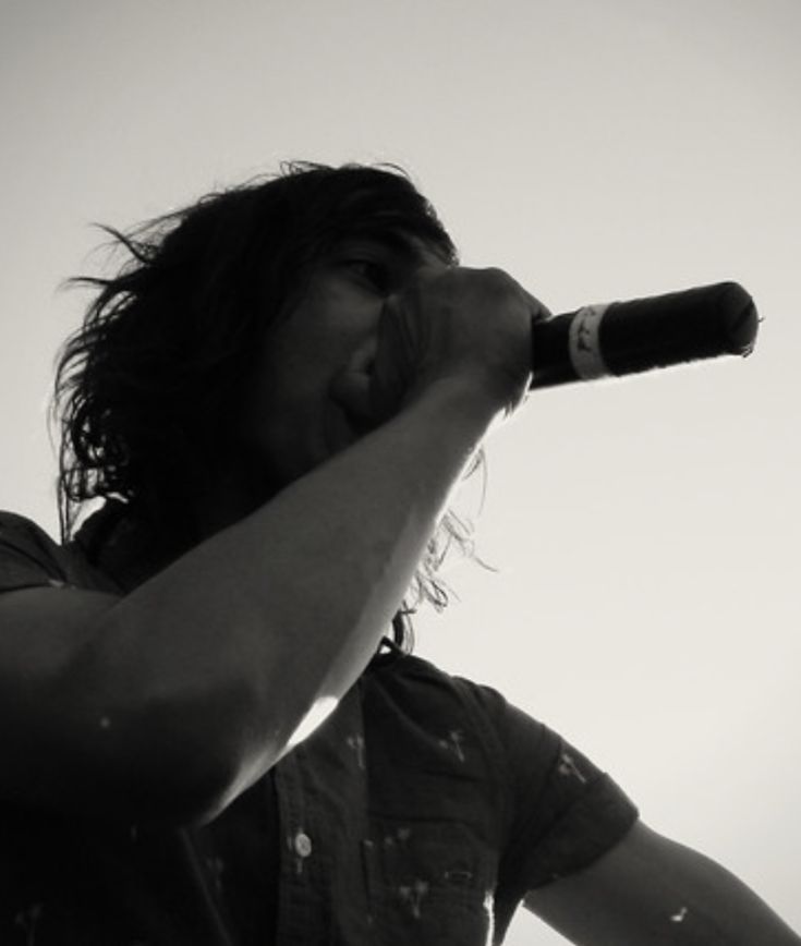 a man with long hair is holding a microphone up to his mouth and singing into it