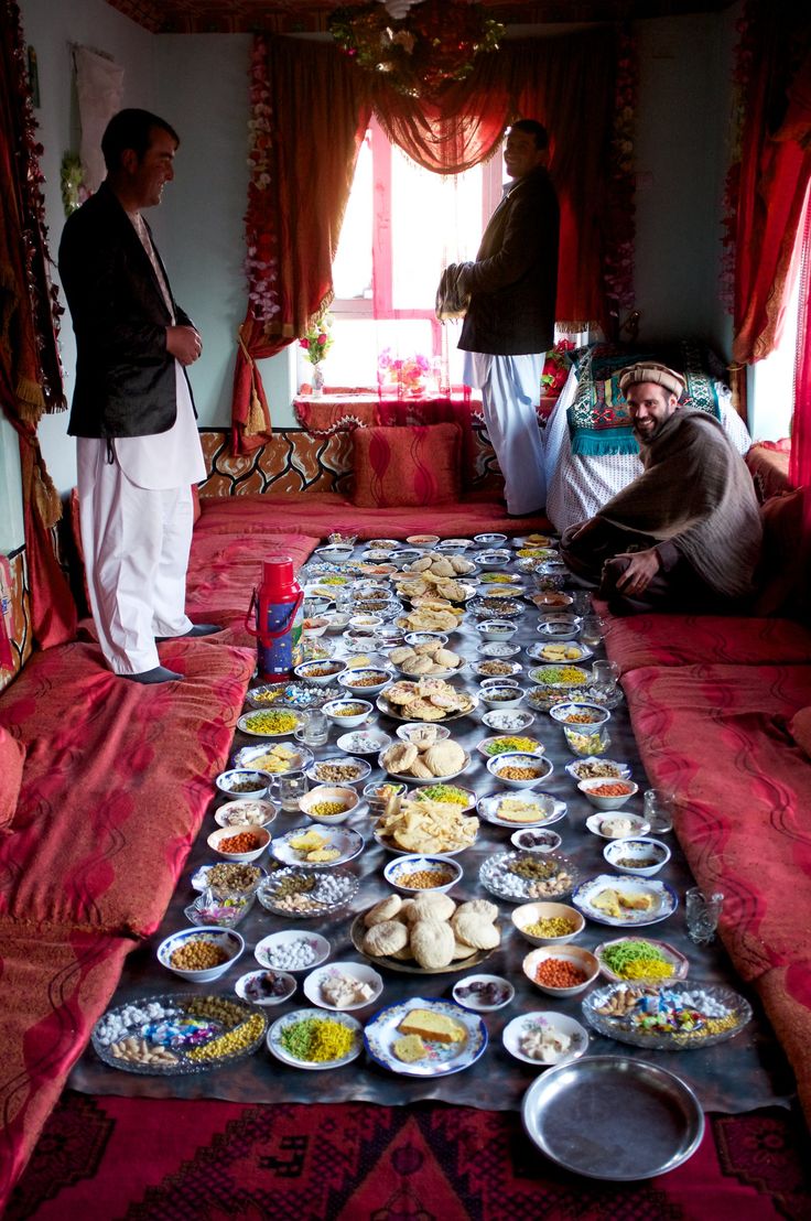 two men standing next to a long table filled with plates and bowls full of food