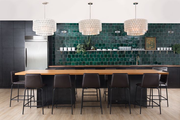 a kitchen with green tiles on the wall and wooden table surrounded by bar stools