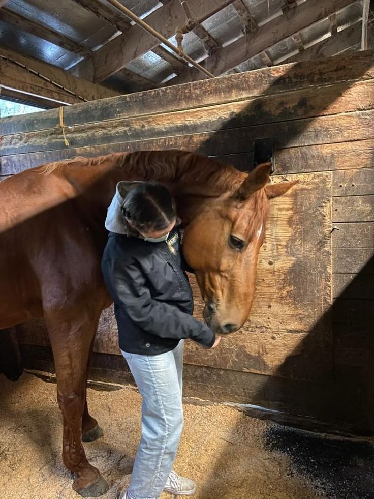 a woman standing next to a brown horse in a barn with it's head on the ground