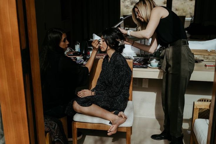 a woman is getting her hair done by two other women at a table in a room