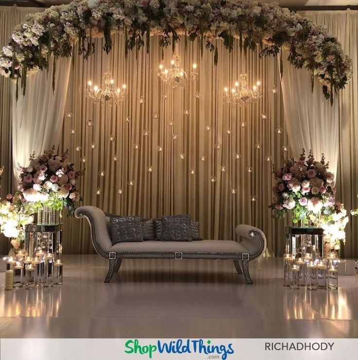 a couch sitting under a chandelier filled with flowers and candles in front of a curtain