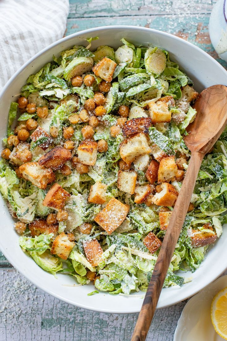 a salad with lettuce and croutons in a white bowl next to a wooden spoon