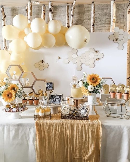 a table topped with lots of yellow and white balloons hanging from the ceiling above it