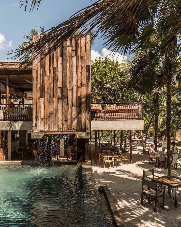 a wooden building sitting on top of a beach next to a swimming pool and palm trees