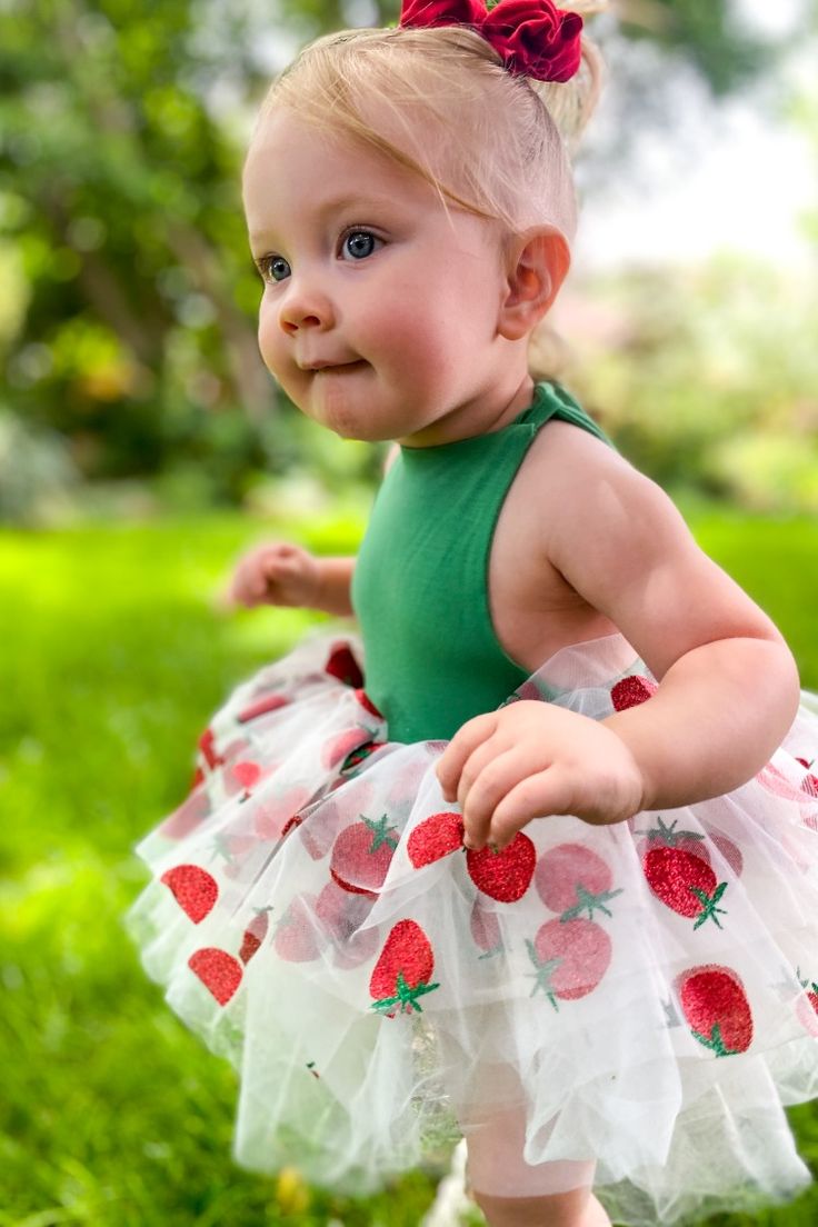 a baby girl wearing a green dress with strawberries on it