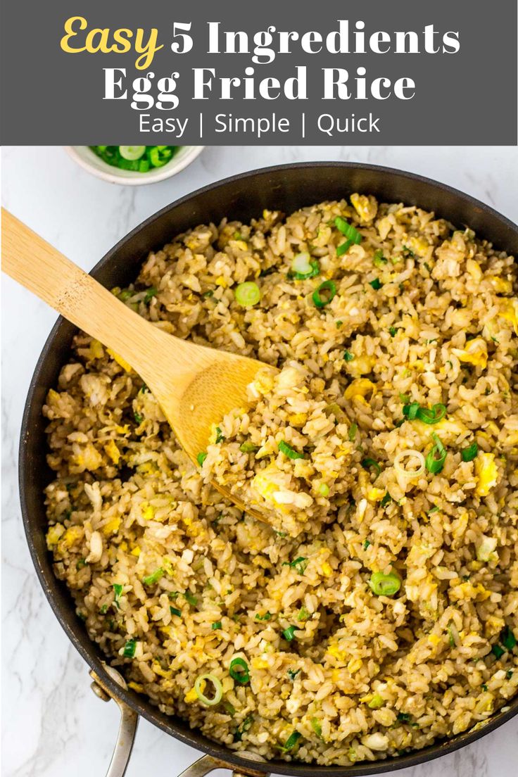 an egg fried rice in a skillet with a wooden spoon and green onions on the side