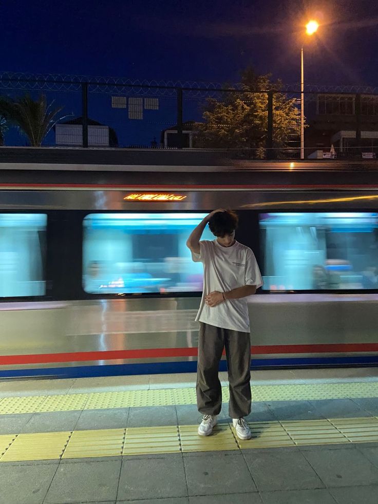 a man standing in front of a train at night with his hand on his head