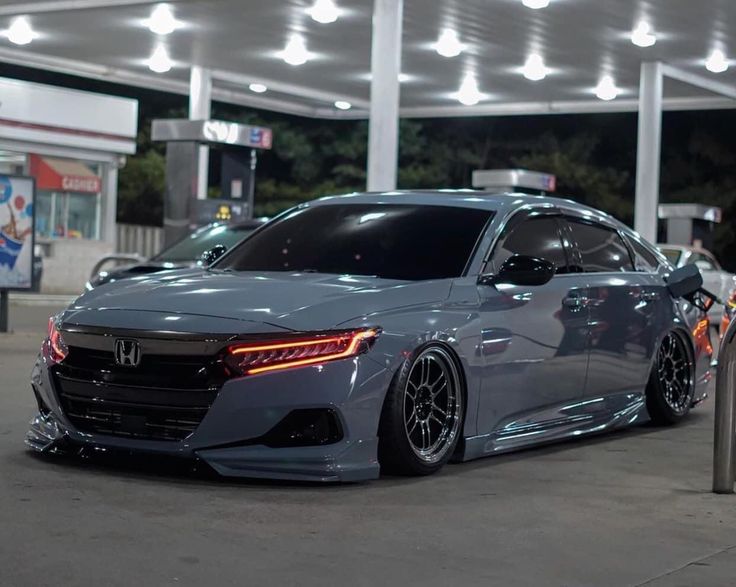 a gray car is parked in front of a gas station at night with its lights on