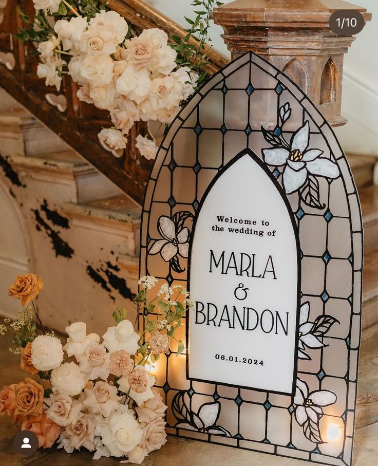 a stained glass window with flowers and candles on the ground next to it is a sign that says marla and brandon