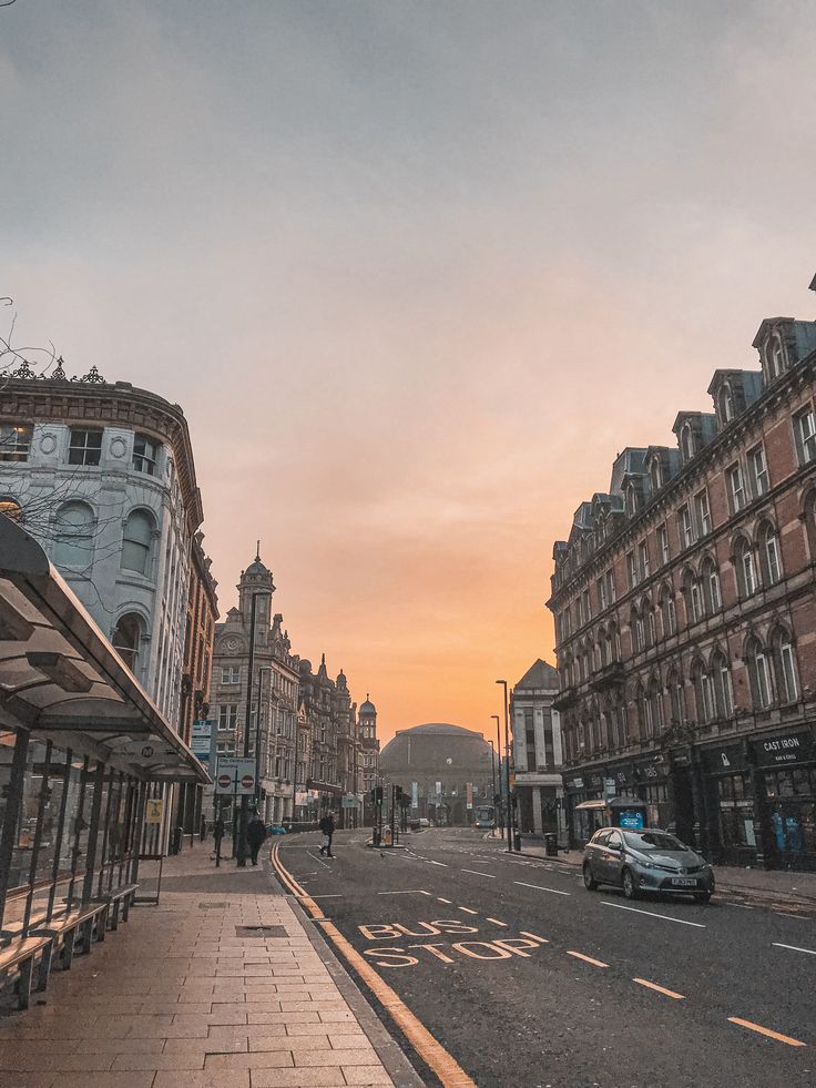 the sun is setting on an empty city street with cars parked along the side of the road