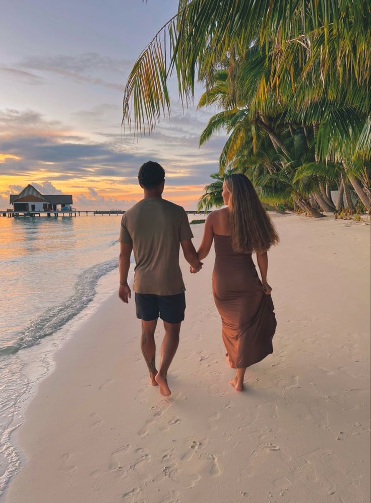 a man and woman walking down the beach holding hands