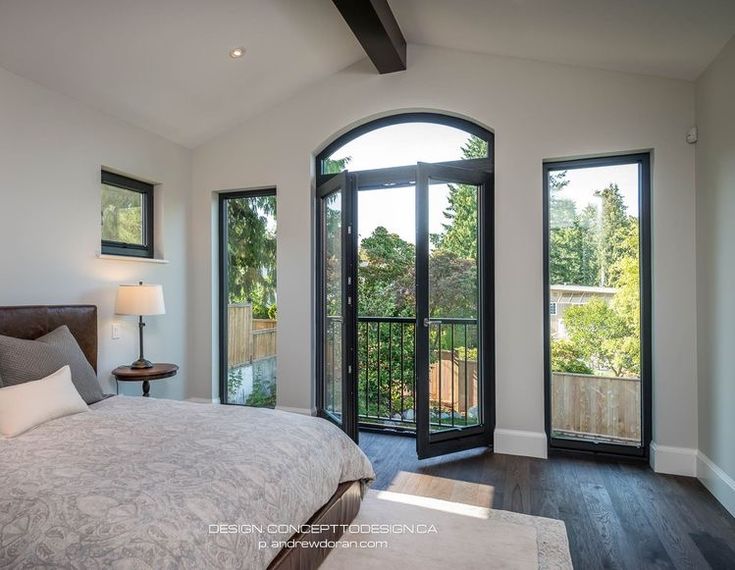 a bedroom with an arched glass door leading to a balcony and deck area that overlooks the trees