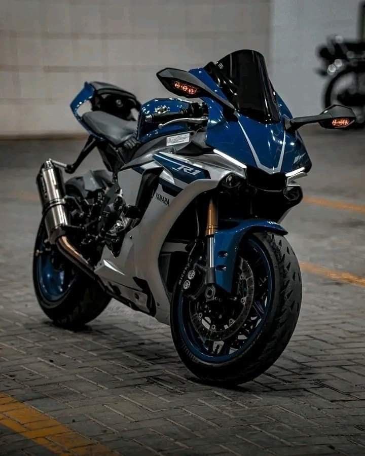 a blue and silver motorcycle parked in a parking lot next to a building on a brick road