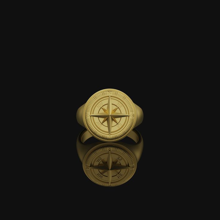 a gold compass ring sitting on top of a black surface with water reflecting in it