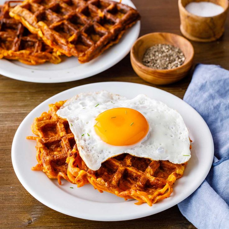 two white plates topped with waffles and an egg