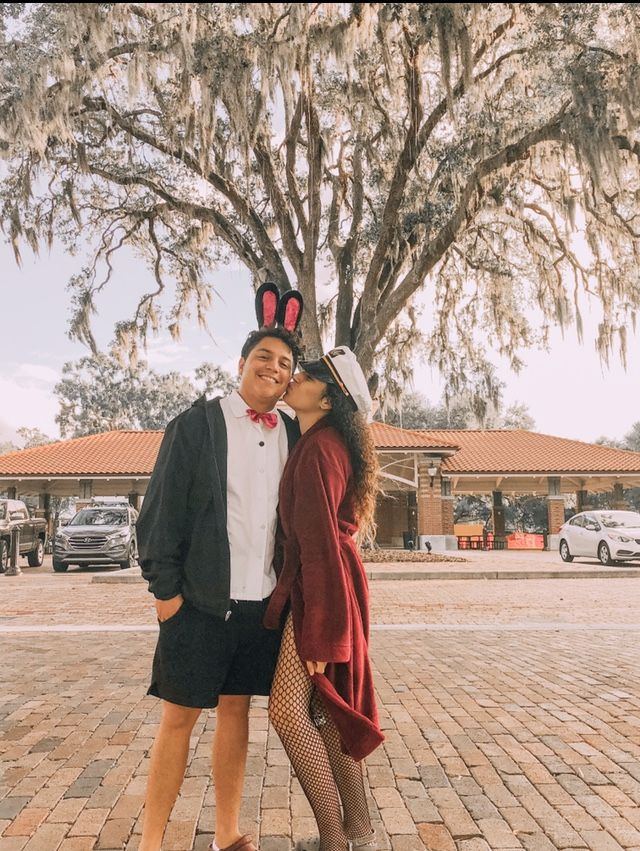 two people dressed up in costumes standing next to each other on a brick walkway under a tree