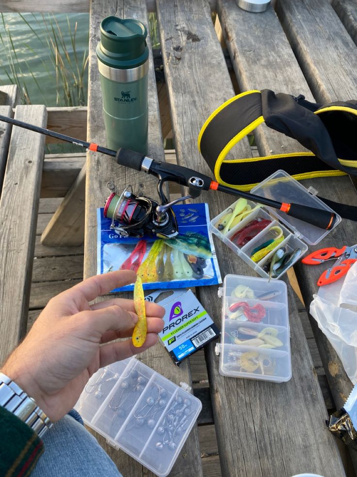 a person holding a fishing rod next to other items on a picnic table