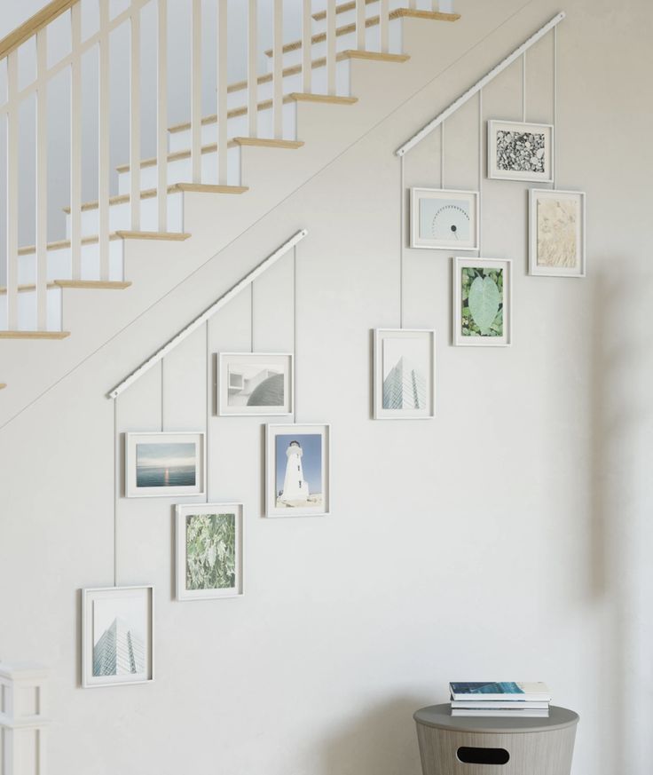 a white staircase with pictures on the wall and a trash can under it next to a stair case