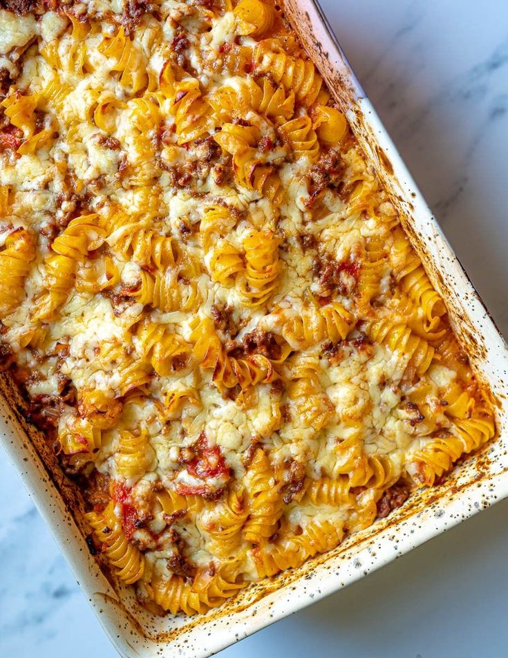 a casserole dish filled with pasta and meat on a marble counter top, ready to be eaten