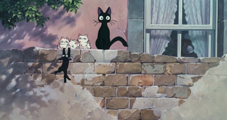 a black cat standing on top of a brick wall next to a group of cats