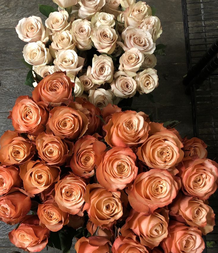 an arrangement of peach and white roses in a vase on top of a wooden table