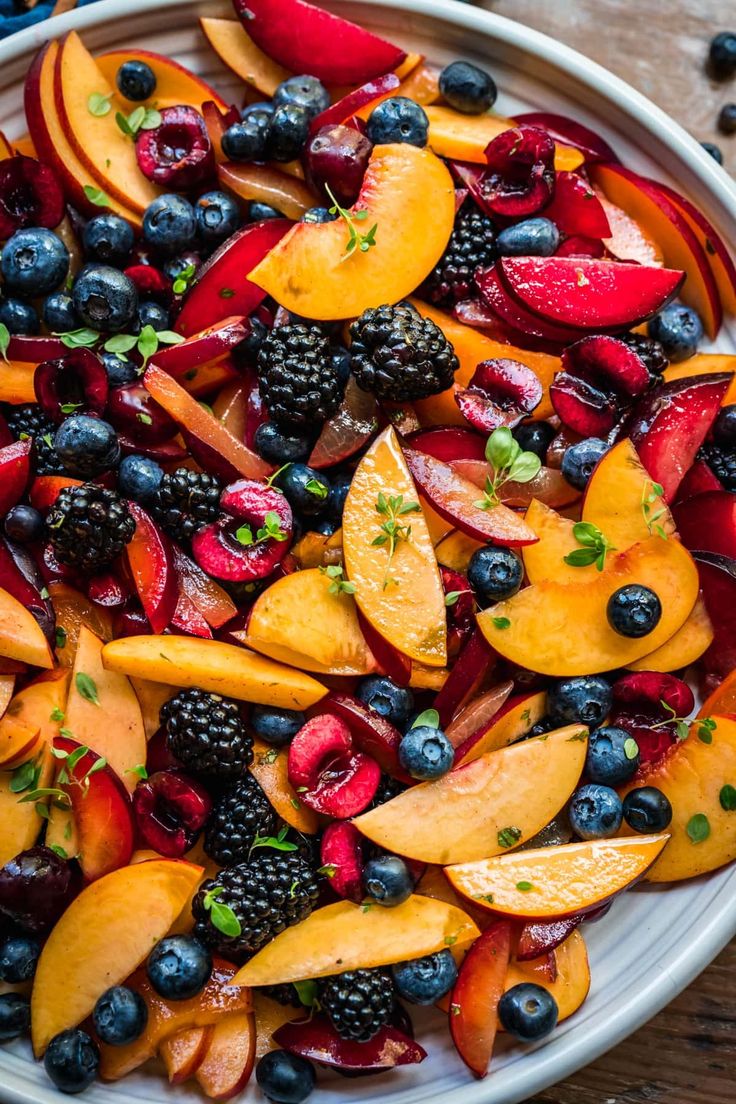 a white bowl filled with sliced fruit and berries on top of a wooden table next to blueberries