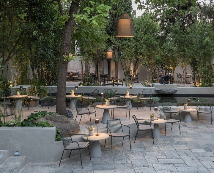 an outdoor dining area with tables, chairs and benches next to trees in the background