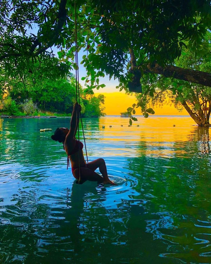 a man hanging from a tree in the water with his feet up on a rope