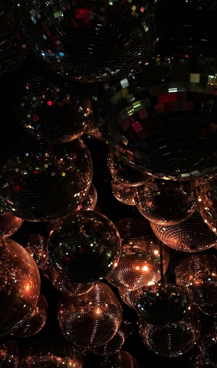 many shiny disco balls are stacked on top of each other in the dark, with lights reflecting off them