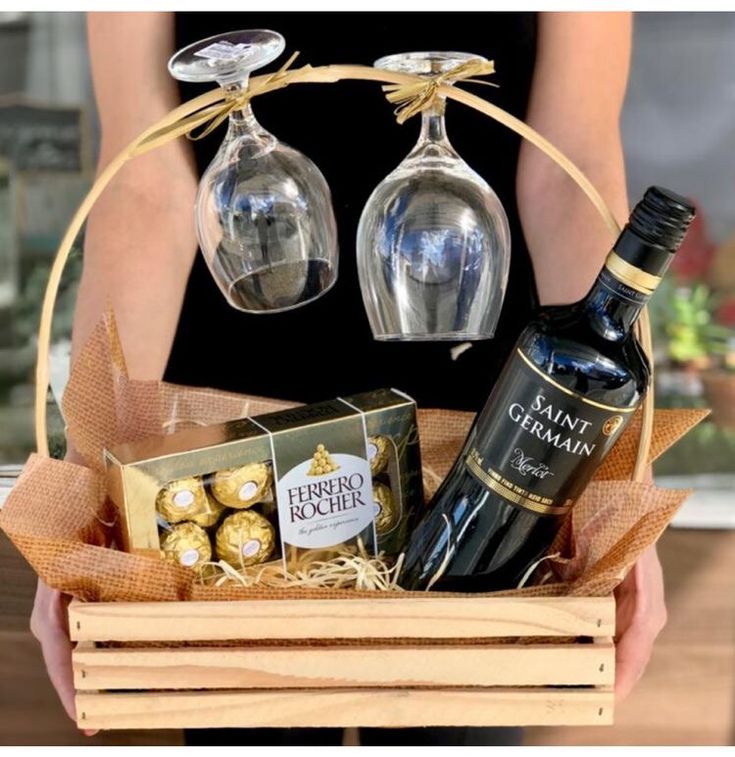 a person holding a basket with two wine glasses and chocolates