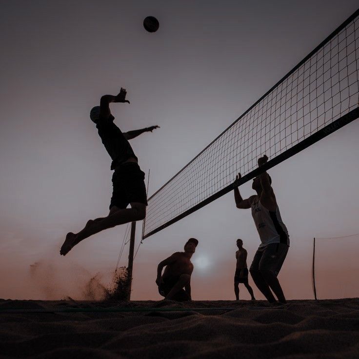 four men playing volleyball on the beach at sunset