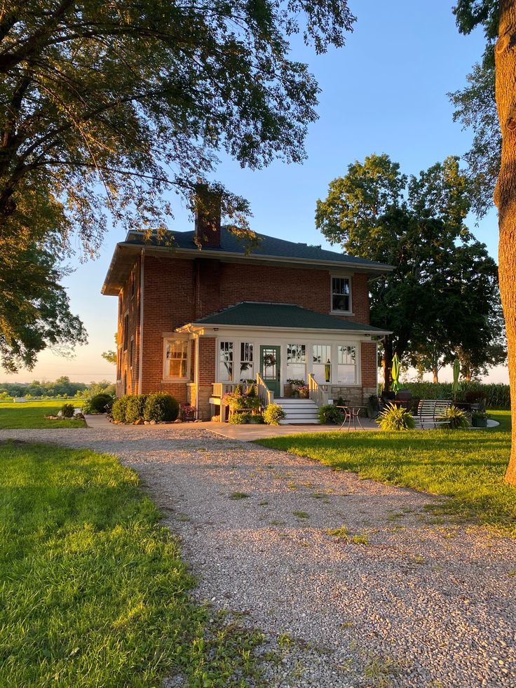 a large red brick house sitting on top of a lush green field next to a tree