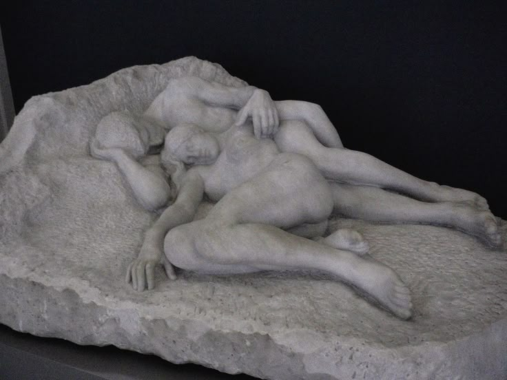 a sculpture of two people laying on top of a rock